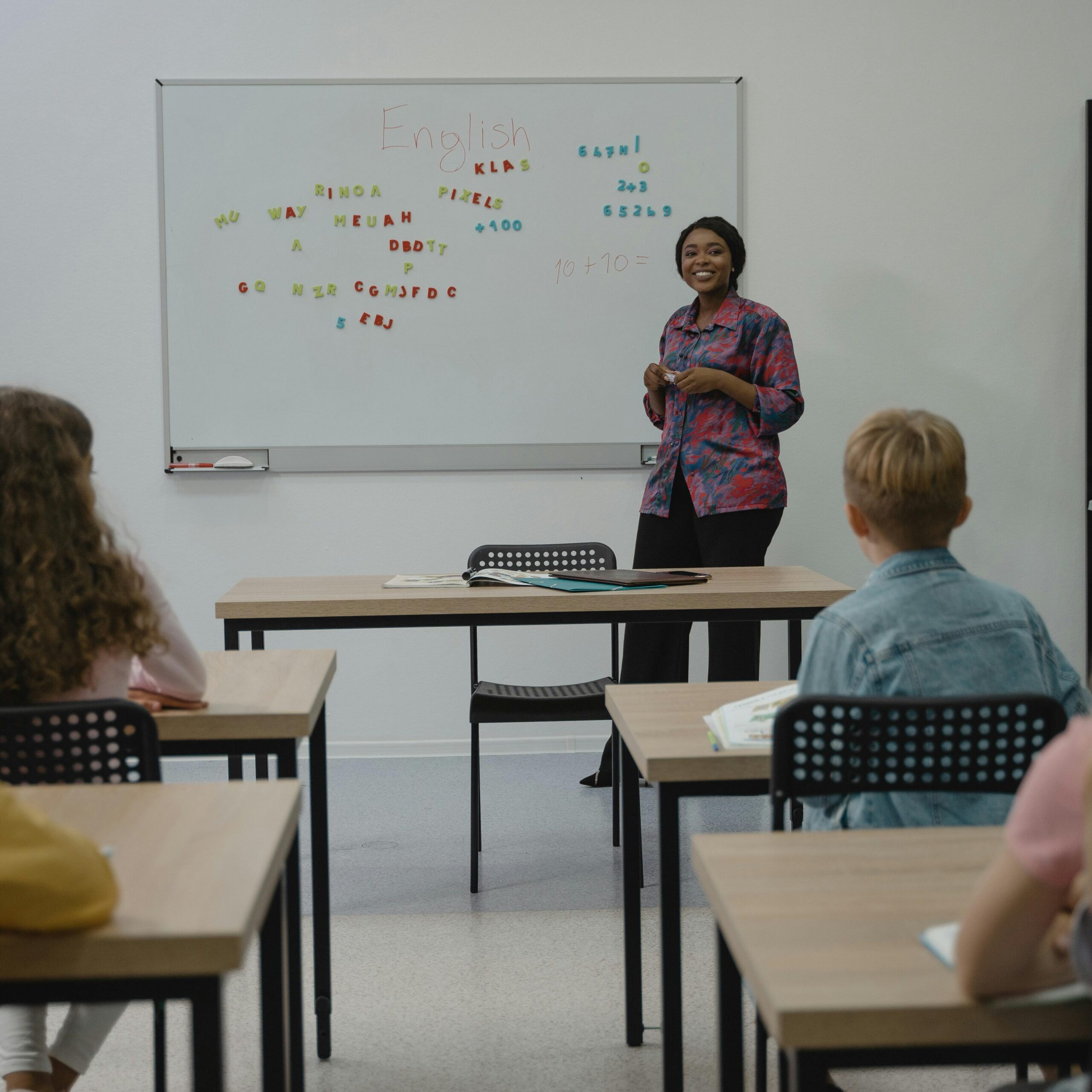 A diverse group of students in an English class with a smiling teacher at the whiteboard.